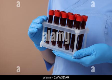 Laboratory testing. Doctor with blood samples in tubes on light brown background, closeup Stock Photo