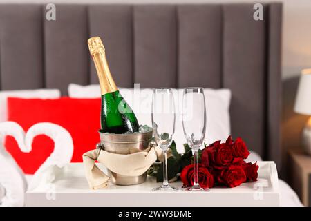 Honeymoon. Sparkling wine, glasses and bouquet of roses on table in room Stock Photo