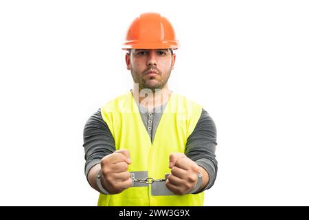 Corrupted adult male constructor in handcuffs wearing safety hardhat and fluorescent vest as work attire isolated on white studio background Stock Photo