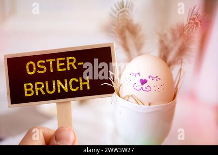 March 21, 2024: Hand holding sign with inscription: Easter brunch, in front of an egg painted as an Easter bunny. PHOTOMONTAGE *** Hand hält Schild mit Aufschrift: Osterbrunch, vor ein als Osterhase bemaltes Ei. FOTOMONTAGE Stock Photo