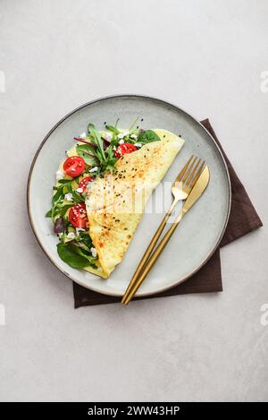 Omelette with herbs, feta cheese and cherry tomatoes on a plate on a light background, top view Stock Photo