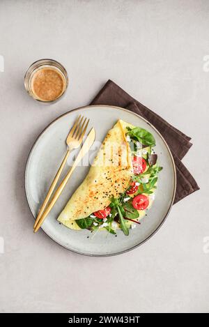 Omelette with herbs, feta cheese and cherry tomatoes on a plate on a light background, top view Stock Photo