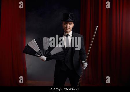 Magician performing miracle trick on stage using fan and cane Stock Photo