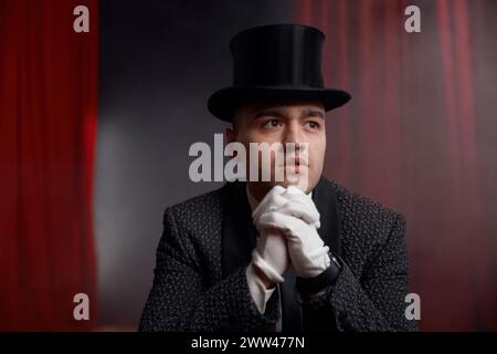 Magician wearing top hat and tuxedo suit holding magic cards in hands Stock Photo