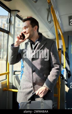 Man in grey coat standing in modern tram, talking on mobile phone wit smile. Fast and convenient way of transportation Stock Photo