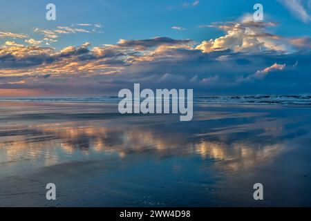 Early morning image of clouds and sky reflecting off the wet beach and shallow water at low tide. Stock Photo