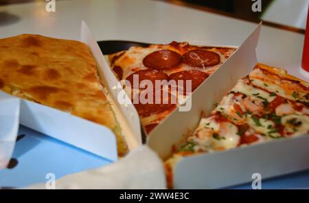 Close-up of three slices of different types of pizza in white triangular paper containers Stock Photo