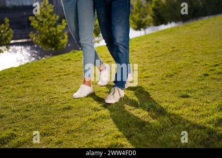 Cropped photo of two partners legs shadow footwear ad walking green grass fresh air free time outside Stock Photo