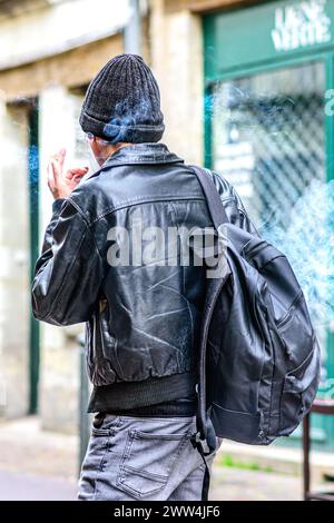 Man in black clothing (rear view) smoking carrying backpack over one shoulder - Tours, Indre-et-Loire (37), France. Stock Photo
