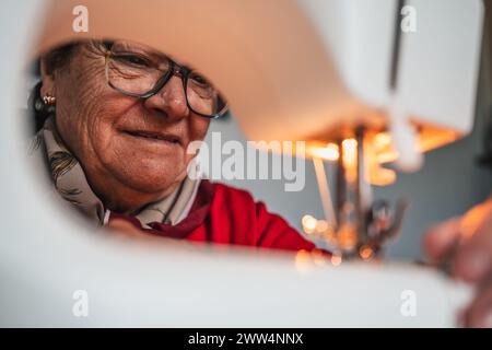 detail portrait face of seamstress woman with glasses using sewing machine while working Stock Photo