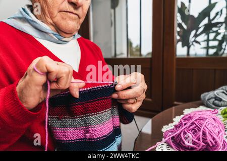 Detail portrait of seamstress woman hands sewing colorful handmade woolen clothes next to the window Stock Photo