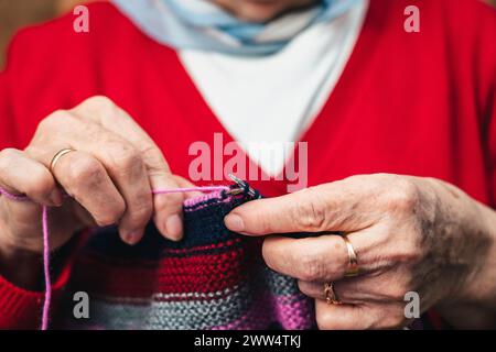detail of hands of senior woman seamstress sewing handmade clothes with colorful wool knit Stock Photo