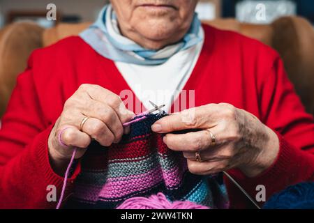 detail of hands of senior woman seamstress sewing handmade clothes with colorful wool knit Stock Photo