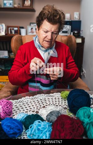 portrait of senior woman and movement of her hands sewing with needles and colored wool on a sofa at home Stock Photo