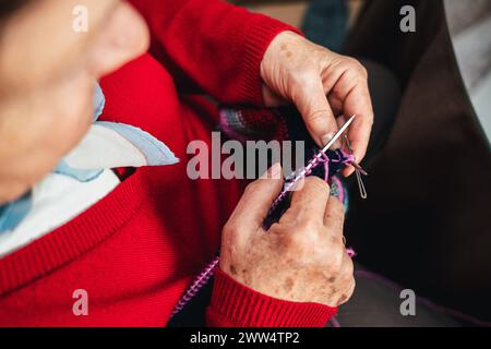 low angle horizontal portrait of senior woman's hands sewing clothes by hand with needles and colored wool Stock Photo