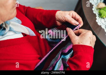 low angle horizontal portrait of senior woman's hands sewing clothes by hand with needles and colored wool Stock Photo