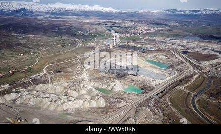 Aerial view of working mine pit. Drone shot of coal mining activity. Artificial polluted lakes. Mountains with snow in the background. Stock Photo