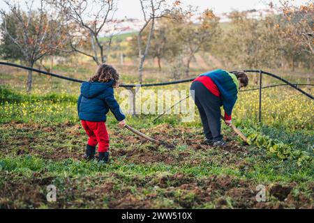little boy helping his grandmother with garden work, learning to grow plants with a hoe Stock Photo
