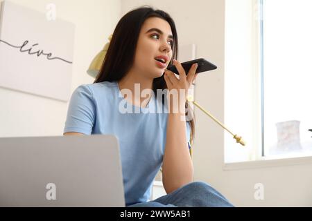 Female freelancer with mobile phone recording voice message in bedroom Stock Photo