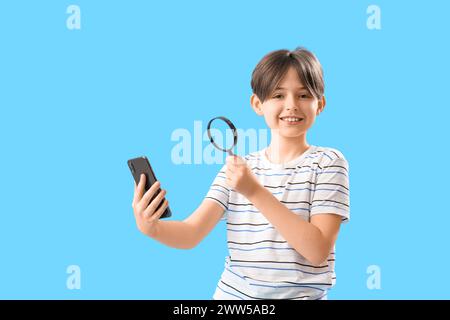 Little boy with mobile phone and magnifier on blue background Stock Photo