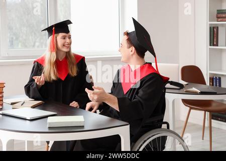 Male graduate in wheelchair chatting with classmate at university Stock Photo