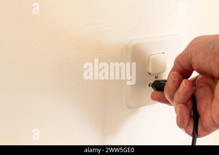 Hand plugging in a power plug into a power outlet on a wall. Power outlet is combined with a switch for switching on the light. Stock Photo
