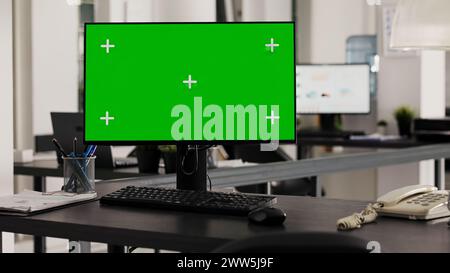 Empty desk with computer shows greenscreen on monitor, running blank mockup copyspace in business office. Workstation in open floor plan office with pc and isolated chromakey template. Stock Photo