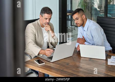 Two busy business men working using laptop computer in office sitting at desk. Stock Photo