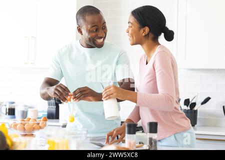 A diverse couple is cooking together in a bright kitchen at home, making eggs Stock Photo