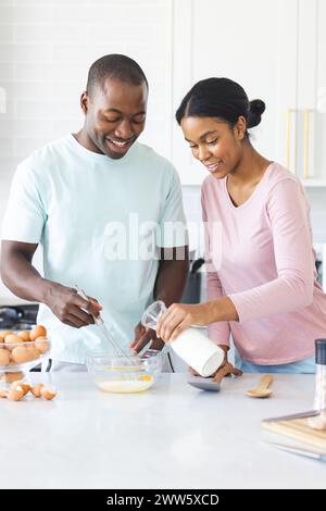 A diverse couple is preparing a meal together, making eggs, in a bright kitchen at home Stock Photo