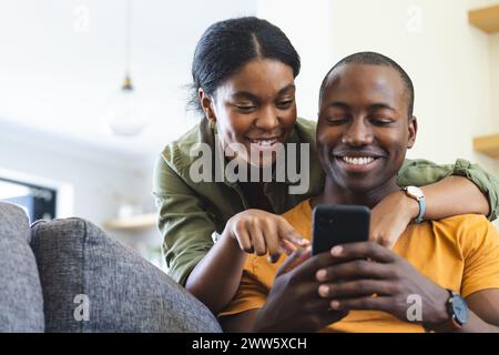 A diverse couple is using a smartphone on the couch at home Stock Photo