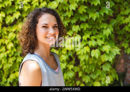 A young Caucasian woman smiles outdoors, green foliage background with copy space Stock Photo