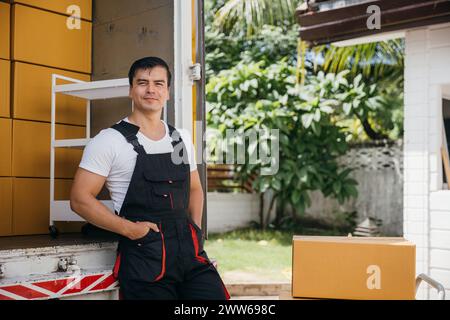 Portrait of a joyful mover working unloading boxes from a truck into a new home. These workers Stock Photo