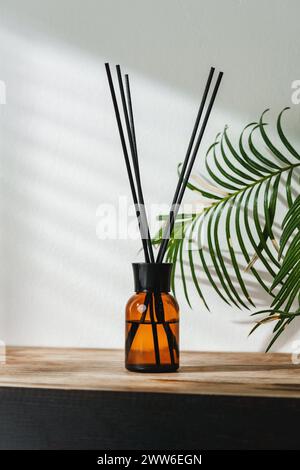 Aromatic Reed Diffuser on Wooden Table With Vibrant Green Leaves Against White Background Stock Photo