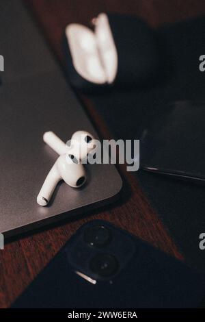 A pair of sleek, white, wireless earphones rest on a silver laptop with a black keyboard. The earphones are designed for comfort and style. Stock Photo