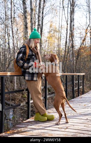 Woman pet owner enjoying walking standing near fence in nature park holding dog's paws.  Stock Photo