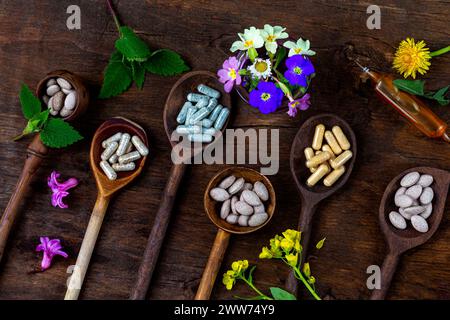 Natural medicine-Capsules, pills, ampoule and medicinal plants seen from above, in wooden spoons. Stock Photo
