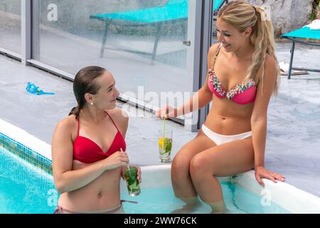 Two friends by the pool, in bathing suits quenching their thirst. Stock Photo