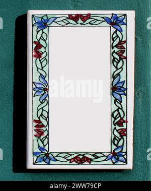 collage, pottery sign in enamel or clay on a rustic turquoise wall. blue, red flowers, green leaves are drawn with pattern. rectangular stone slab. Stock Photo