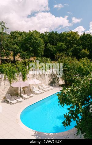 White sun loungers stand on the shore of an oval pool in a green garden Stock Photo