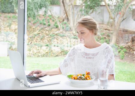 Woman Having Salad whilst Using Laptop Computer Stock Photo