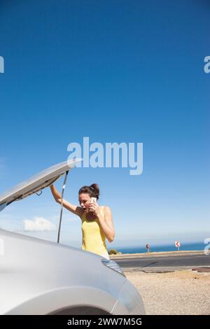 Woman Looking under Car Hood whilst Talking on the Phone Stock Photo