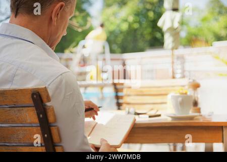 Back View of  Man Writing on Notepad at Outdoors Cafe Stock Photo