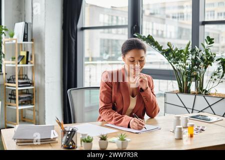 happy african american nutritionist evaluating medication while writing notes in her office Stock Photo