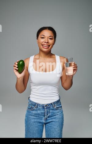 happy african american nutritionist promoting hydration and healthy eating with avocado and water Stock Photo