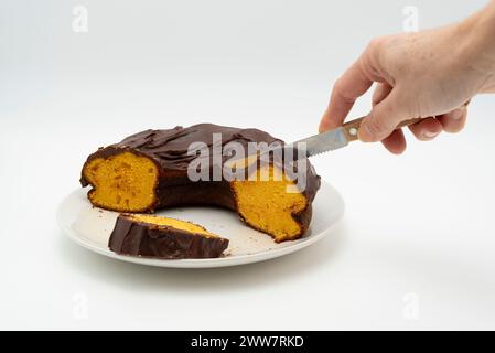 Hand cutting with knife delicious and traditional Brazilian Carrot Cake isolated on white background. Stock Photo