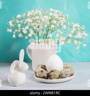 Quail eggs, ceramic bunny, white gypsophila on white table. Holiday Easter decorations and symbols still life. Easter card in white turquoise colors. Stock Photo