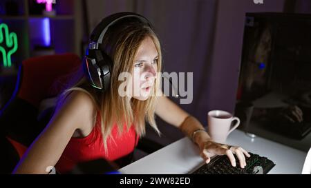 Focused young woman with headphones using computer in a dark gaming room Stock Photo