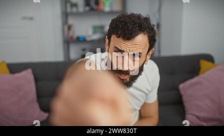 Handsome middle-aged man with beard extending hand towards camera in modern living room. Stock Photo