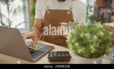 A man in a flower shop counts uae dirhams near a laptop and calculator, indicating business transactions or financial management. Stock Photo